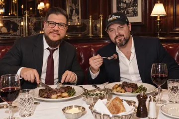 Aaron Rountree and Andrew Lee Jenkins eating steak dinners in a wood-paneled steakhouse booth