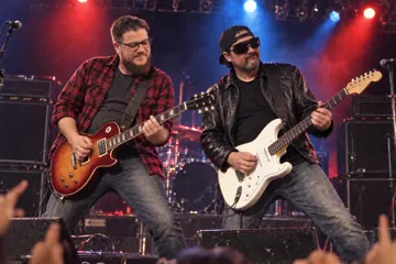 Aaron Rountree and Andrew Lee Jenkins playing electric guitars on a concert stage under red and blue lights