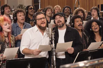 Aaron Rountree and Andrew Lee Jenkins singing at a studio microphone in headphones, surrounded by a large choir
